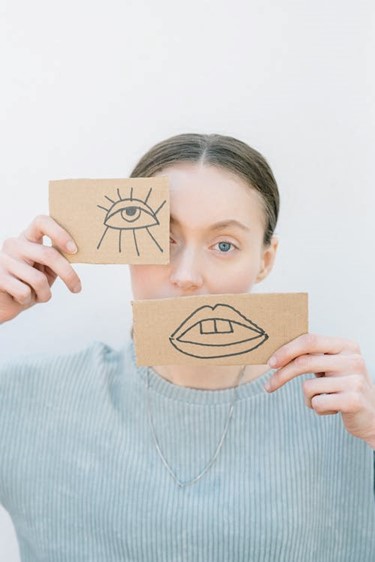 Female holding up image of an eye and mouth drawn on brown cardboard