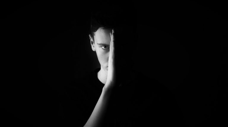 black and white image of young man. we can only see the outline of one hand held up to his face, and the side of his face.