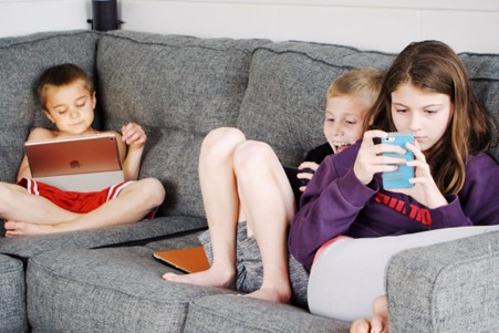 Young children on the sofa on their own tablet or mobile phone