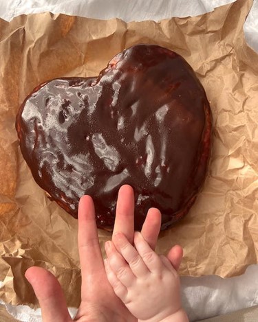 Baby hand on adult hand over chocolate covered heart on brown paper