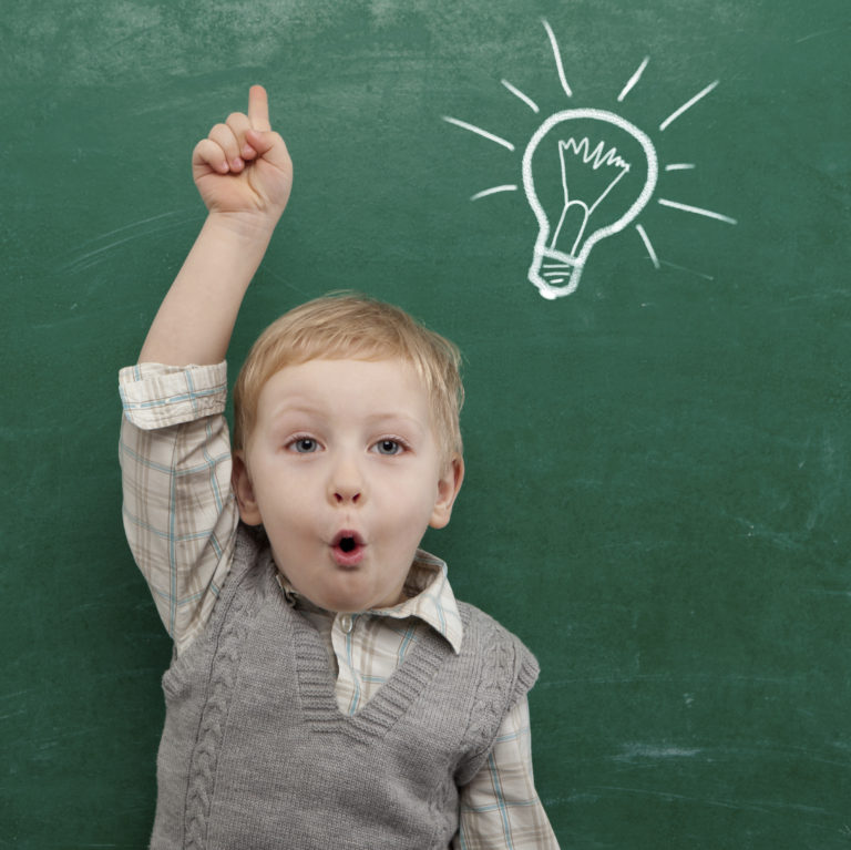 young boy with hand up, in front of a blackboard, a cartoon lightbulb above his head.