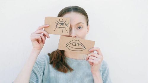 Girl holdin up eye and mouth drawn on cardboard in front of her face
